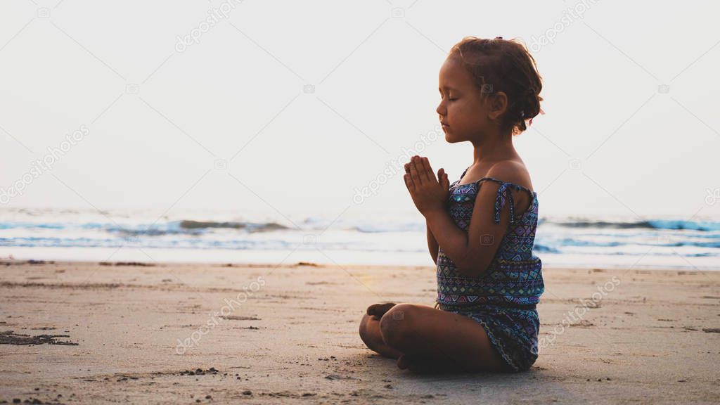 Vintage image of cute little girl meditating on sandy beach