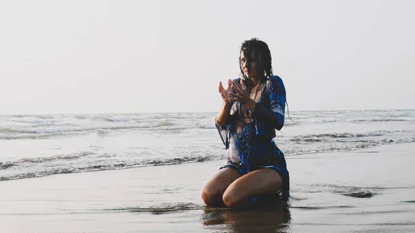 Молодая мокрая женщина сидит в воде на песчаном пляже и практикует медитацию — стоковое фото