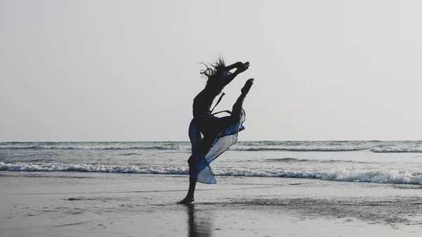 Silhueta de jovem dançando com elementos de ginástica na praia de areia — Fotografia de Stock