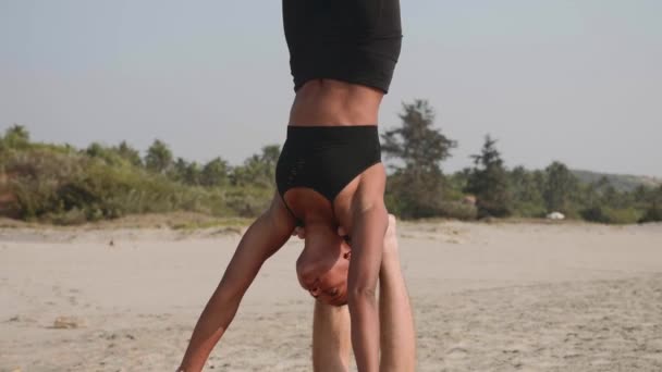 Fit sporty couple practicing acro yoga with partner together on the sandy beach. — Stock Video