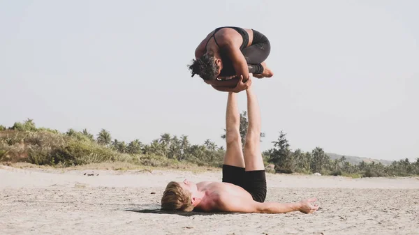 Illeszkedik a sportos pár acro jóga partnerrel együtt a homokos strandon. — Stock Fotó