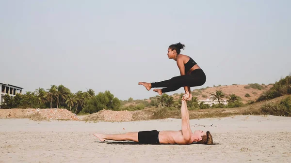 Fit sportovní pár cvičení acro jógy s partnerem společně na písečné pláži. — Stock fotografie