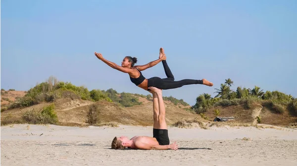 Illeszkedik a sportos pár acro jóga partnerrel együtt a homokos strandon. — Stock Fotó