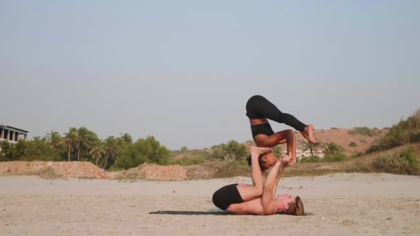 Ajuste pareja deportiva practicando acro yoga con pareja juntos en la playa de arena . — Vídeo de stock