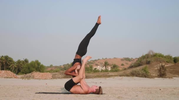 Fit sportieve paar beoefenen van acro yoga met partner samen aan het zandstrand. — Stockvideo