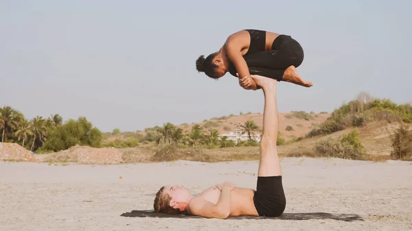 Illeszkedik a sportos pár acro jóga partnerrel együtt a homokos strandon. — Stock Fotó