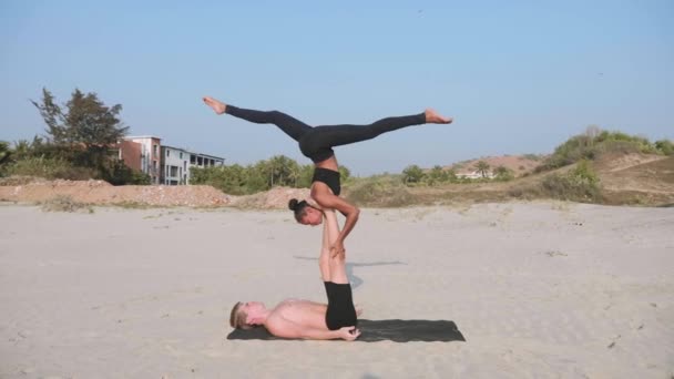 Apto casal desportivo praticando acro ioga com parceiro juntos na praia de areia . — Vídeo de Stock