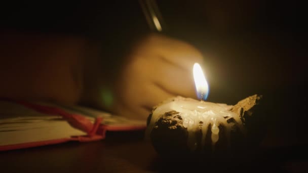 Close-up da menina criança está escrevendo por caneta à luz de velas no quarto escuro — Vídeo de Stock