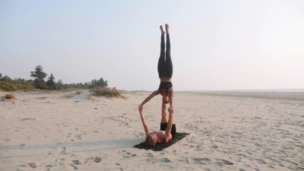 适合运动的夫妇练习阿克罗瑜伽与合作伙伴一起在沙滩上. — 图库视频影像