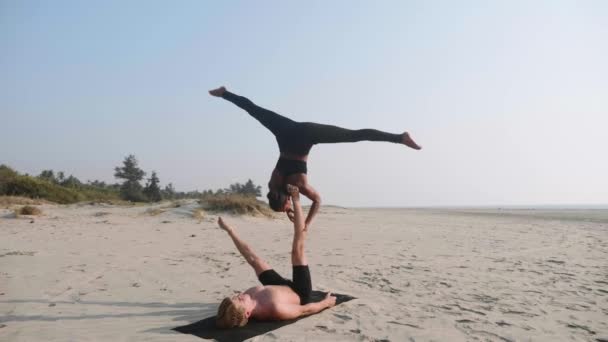 Passa sportig par öva acro yoga med partner tillsammans på sandstranden. — Stockvideo