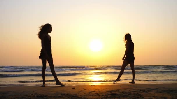 Silhouet van sportieve jonge vrouwen beoefenen van acrobatische element op het strand. — Stockvideo