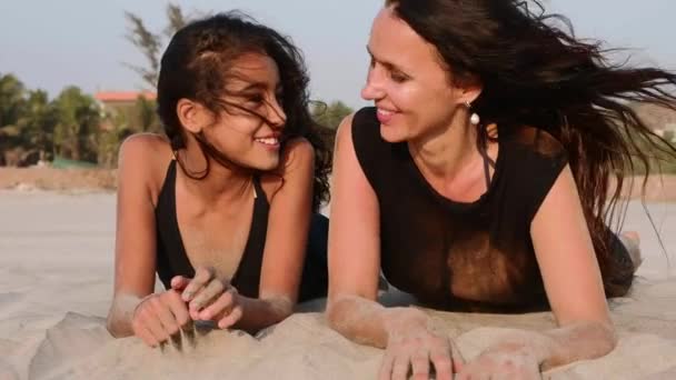 Мать и дочь-подросток лежат вместе на песчаном пляже, разговаривают и смеются — стоковое видео