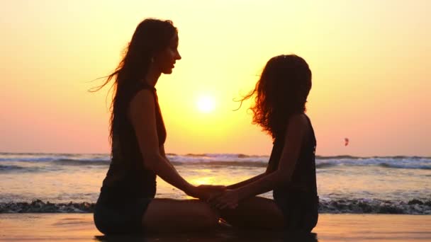 Mamá e hija están sentadas juntas en la playa con las manos cogidas al atardecer — Vídeo de stock