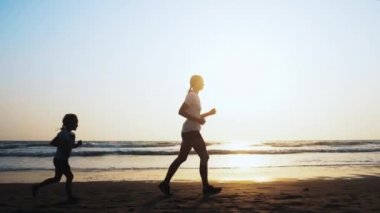 Anne ve kızı gün batımında deniz kumu plajda jogging vardır.