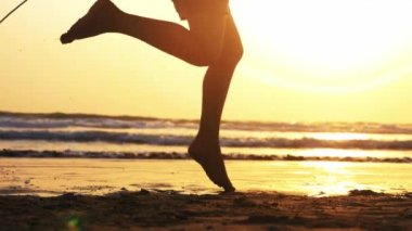 Güneş batımında deniz kumu plajda ip atlama kız bacaklar silüeti.