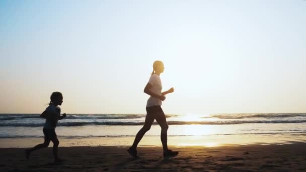 Maman et sa fille font du jogging sur la plage de sable marin au coucher du soleil . — Video