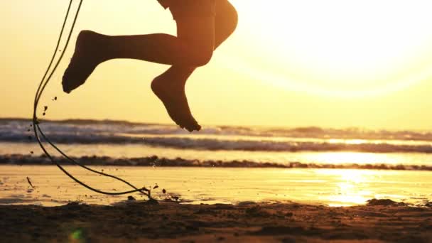 Silhouet van meisjes benen springen op het touw op de zee zandstrand bij zonsondergang. — Stockvideo