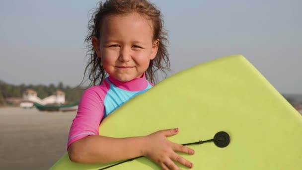 Πορτρέτο του μικρού κοριτσιού σέρφερ με μια σανίδα του σερφ στα χέρια της στην παραλία. — Αρχείο Βίντεο