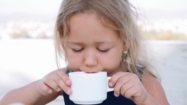 Niña rubia está bebiendo cacao de la taza blanca . — Vídeos de Stock