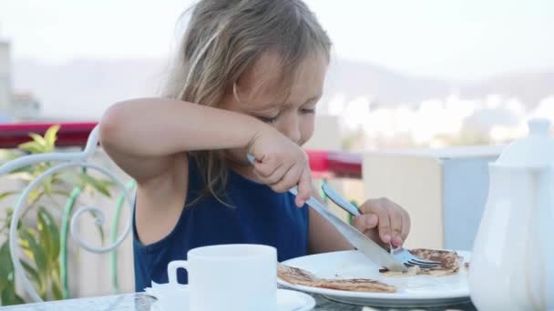 Portréja kislány vágás a palacsinta, és enni reggelire. — Stock videók