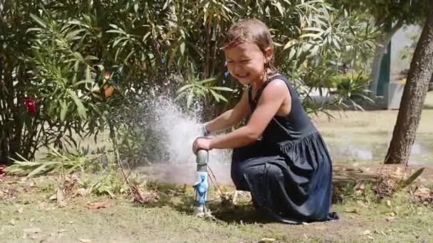 Lycklig flicka leker med vattenstråle från röret på gräs mattan. — Stockvideo