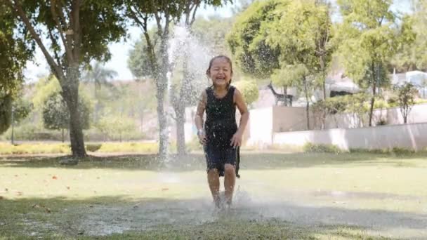 Boldog lány ugró pocsolya a vízsugár a parkban. — Stock videók