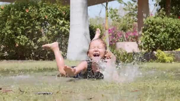 Menina feliz desfrutar de espirrar deitado na poça no gramado no parque . — Vídeo de Stock