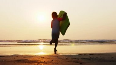 Küçük kız elinde sörf tahtası tutan dalgalar denizde çalışıyor.