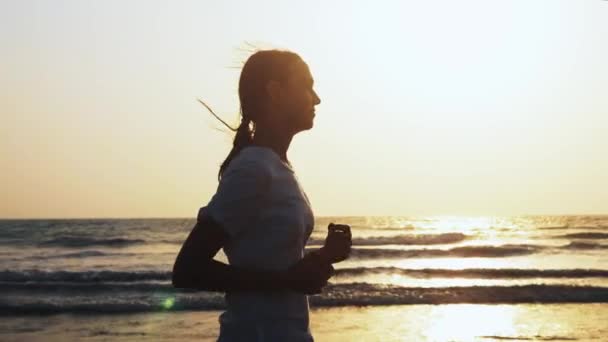 Fit sportig kvinna är jogging på stranden vid solnedgången — Stockvideo