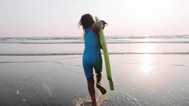 Petite fille court sur la mer aux vagues tenant la planche de surf dans ses mains . — Video