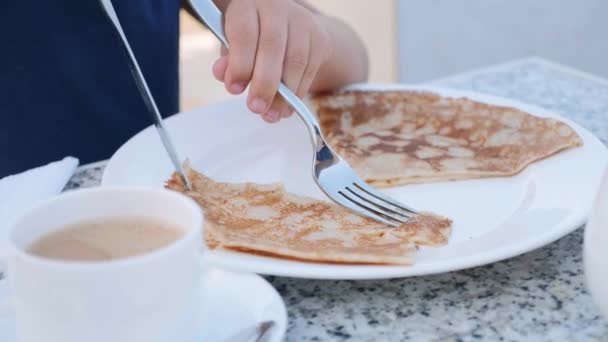 Little girl is cutting a pancake with knife and fork for breakfast. — Stock Video
