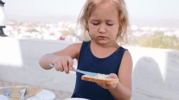 小さな女の子は朝食にバターでサンドイッチを作っています. — ストック動画