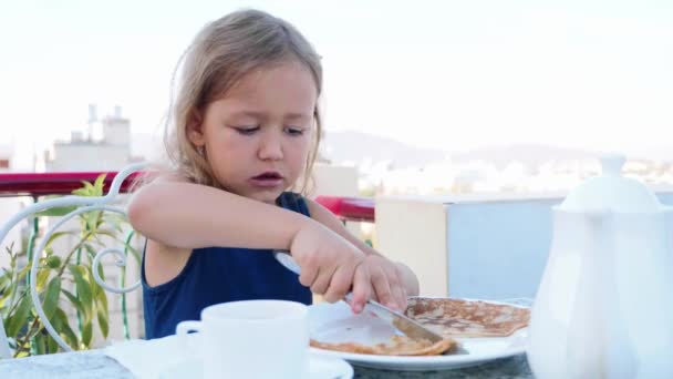 La niña está cortando un panqueque y comiéndolo para el desayuno. . — Vídeos de Stock