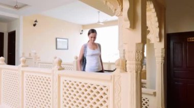 Woman passes into the hotel and rolls the suitcase to her room. Front view.