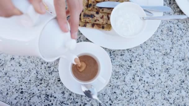Gieten van warme chocolademelk van theepot tot kopje voor ontbijt. — Stockvideo