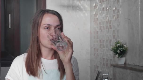 Young woman rinses her mouth with water and looking at mirror. — Stock Video