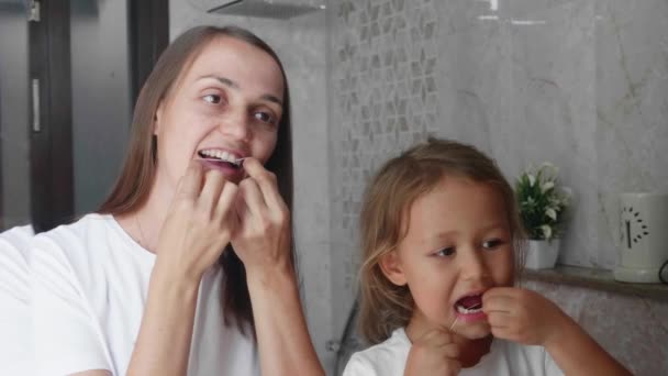 Мама и маленькая дочь чистят зубы зубной нитью в ванной вместе — стоковое видео