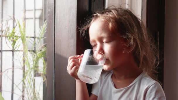 Klein schattig meisje is het drinken van haar drank kijken naar venster. — Stockvideo