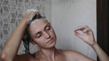 Young woman is washing her hairs with shampoo taking a shower with close eyes.