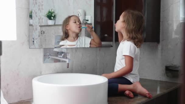 Kleine jongen meisje borstelen haar tanden met tandenborstel voor de spiegel. — Stockvideo