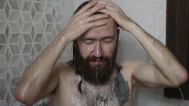 Молодой бородатый мужчина моет голову в душе дома, крупным планом — стоковое видео