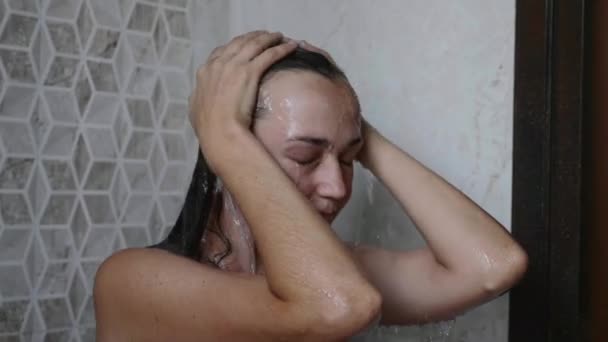 Jeune femme bronzée prend une douche avec les yeux fermés . — Video