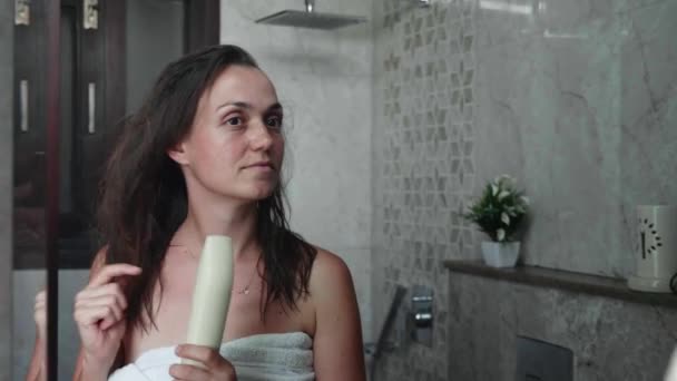 Young woman dries her hair with a hair dryer. Portrait shot in mirror reflection — Stockvideo