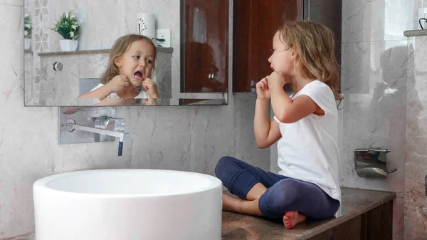 Piccola ragazza carina si lava i denti con filo interdentale davanti allo specchio . Foto Stock