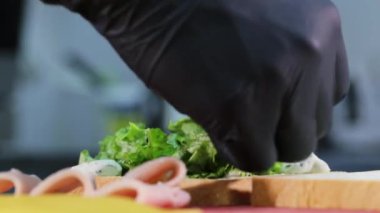 Adam sandviç pişirirken marul ile ekmek üzerine jambon koyar.