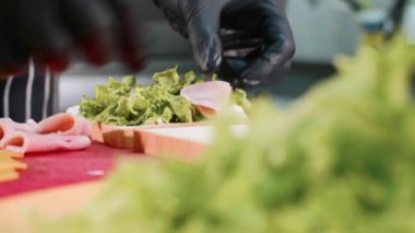 Closeup şefler eller marul, jambon ve peynir ile sandviç pişirme.