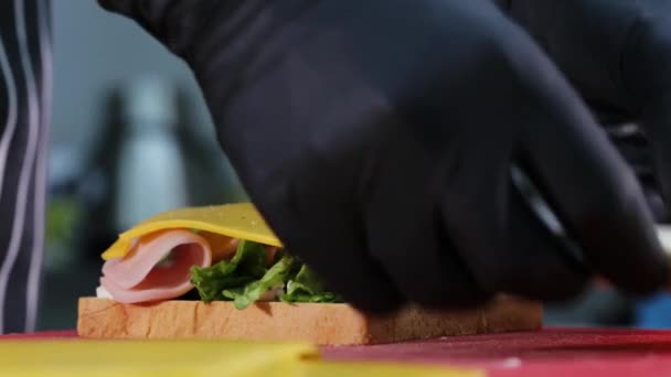 Chef kocht Sandwich mit Schinken, Käse, Salat und zwei Scheiben Brot. — Stockvideo