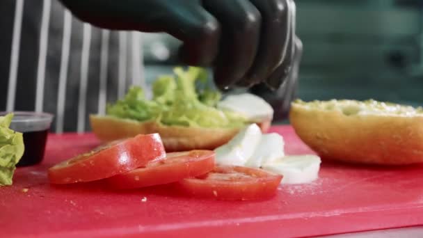 Шеф-повар готовит сэндвич с соусом, моцареллой, салатом и помидорами — стоковое видео