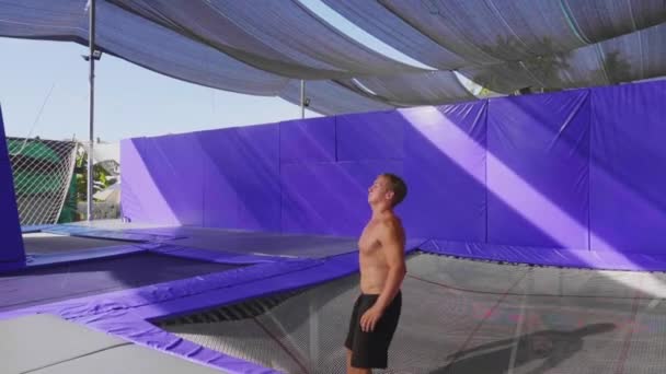 Musculoso hombre gimnasta en pantalones cortos es saltar en trampolín haciendo volver voltereta . — Vídeos de Stock