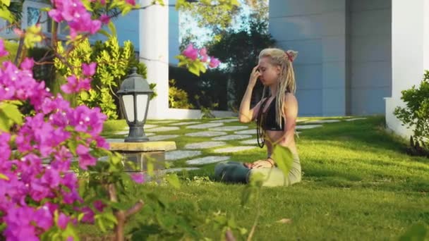 Молода дівчина сидить на газоні і робить практику йоги-дихання Пранаяма — стокове відео